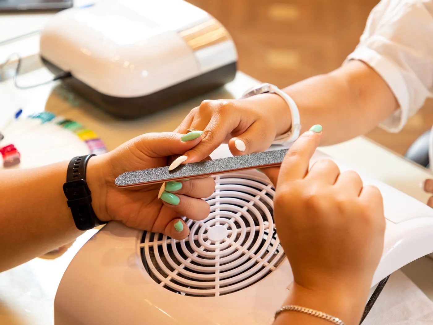 Nail technician shaping and filing a client's nails at a manicure table